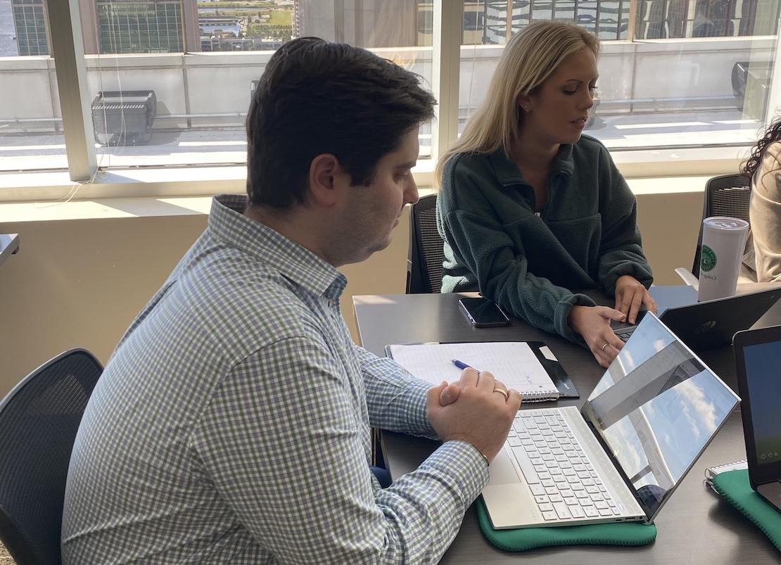 A male and female student sitting a table using their laptops together, seemingly to work on a group project.